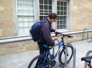 Sophomore Matt Willis pulls his bike from the racks outside O'Shaughnessy Education Center. Willis said the rain makes commuting difficult, but it's better than walking through the snow. (Michelle Doeden/TommieMedia) 
