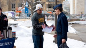 Sophmore Daniel Sedlacek of the Knights of Columbus hands a flag to Anthony Domeier in celebration of Presidents Day. (John Kruger/TommieMedia)