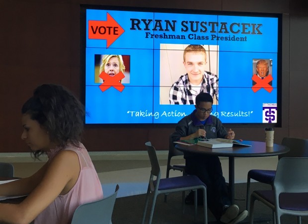 Ryan Sustacek's politically-centered advertisement appears on a screen behind students studying in the Anderson Student Center. Sustacek won the election for freshman class president after running what he called a "relevant" campaign. (Photo Credit: Ryan Sustacek) 