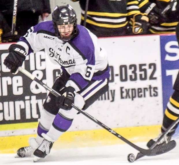 Defenseman Michael Krieg battles for puck posession near the Gustavus bench. Krieg is now pursuing a career with the ECHL. (Jake Remes/TommieMedia) 