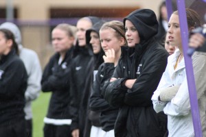 <p>Tommie players stand out in the rain to cheer on their teammates near the end of the game. (Miles Trump/TommieMedia)</p>